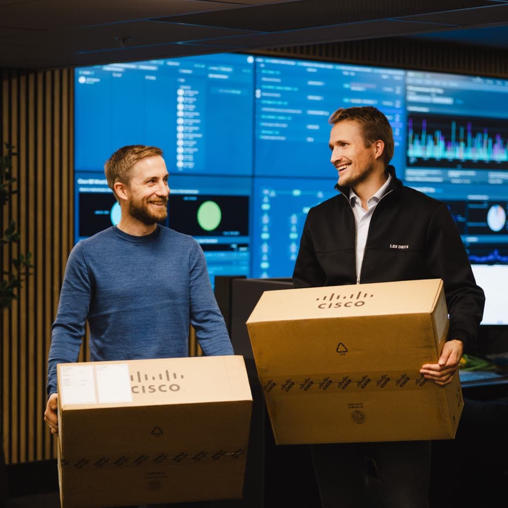 Two people holding Cisco packaging, looking at each other and smiling in a office environment