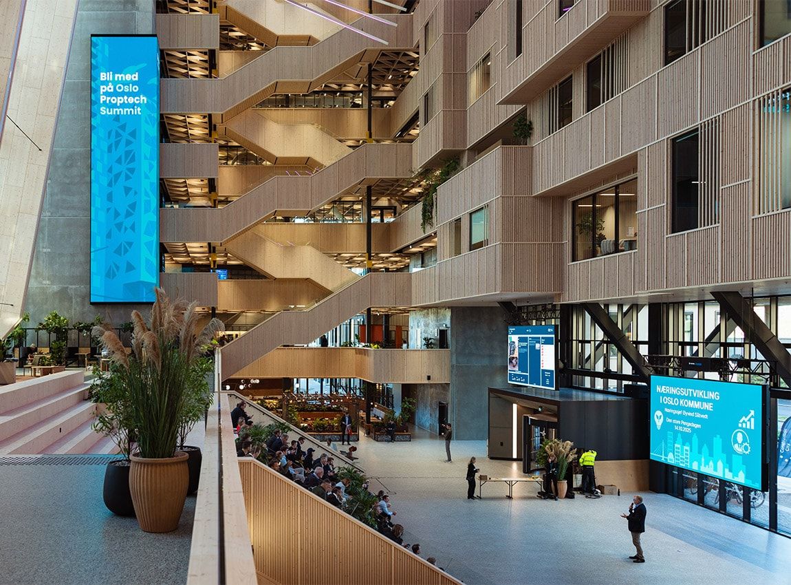 Spacious, modern office atrium with large glass windows, natural light, indoor trees, and people working or socializing.