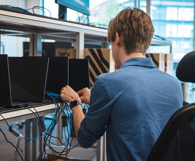 Person connecting cables to laptops at a workstation in an office.