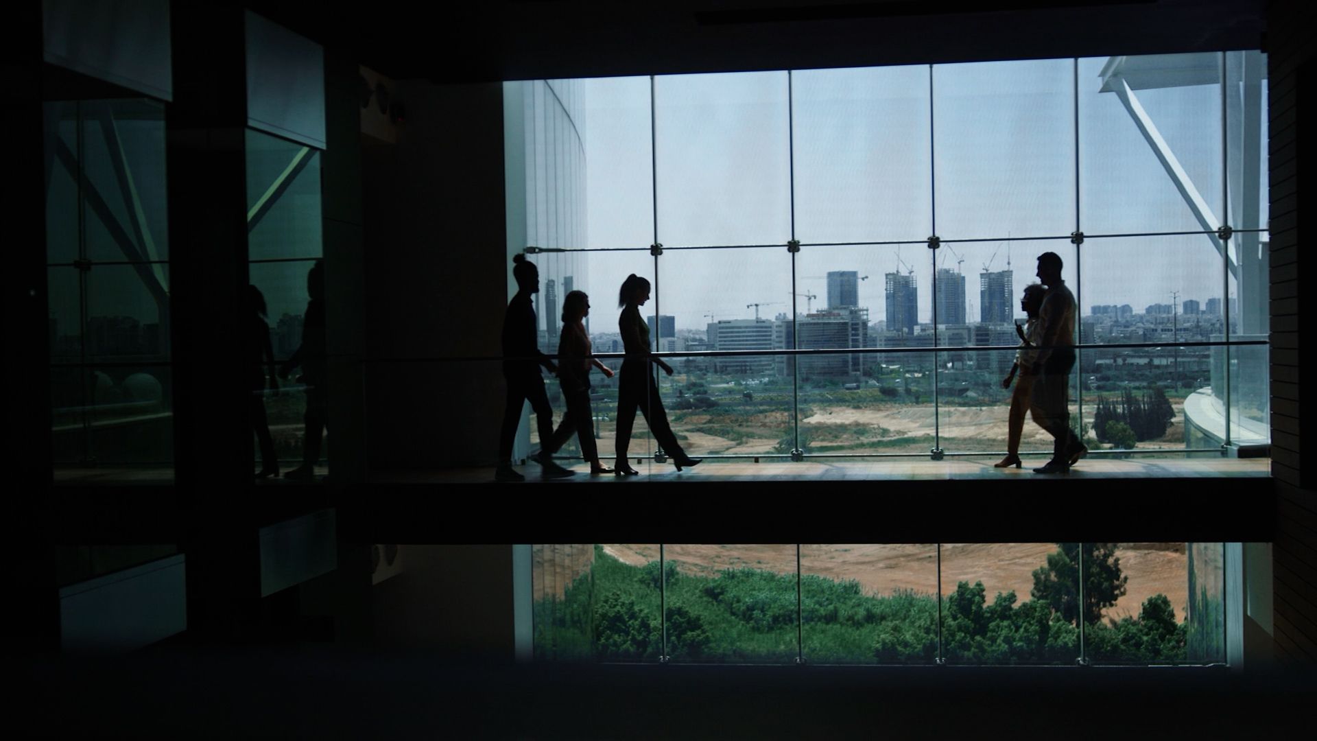 People walking across an indoor bridge in a modern office building. 