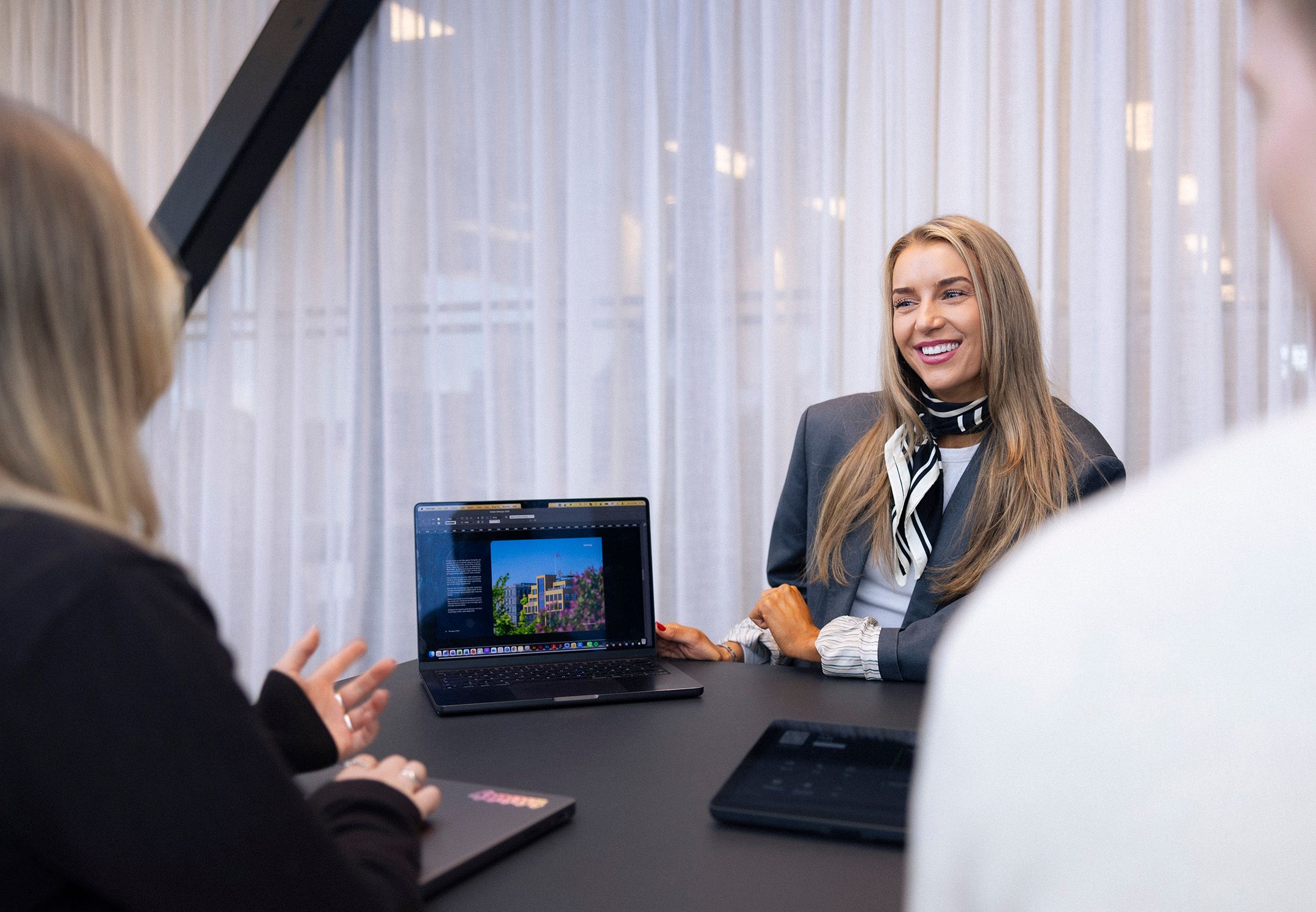 Tre personer i møte rundt et bord, ser på en laptop med et bygningsdesign.
