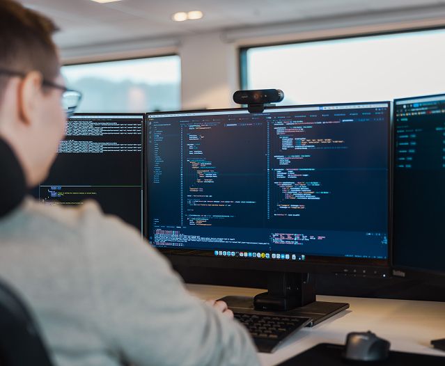 Person coding at a desk with multiple monitors displaying code.