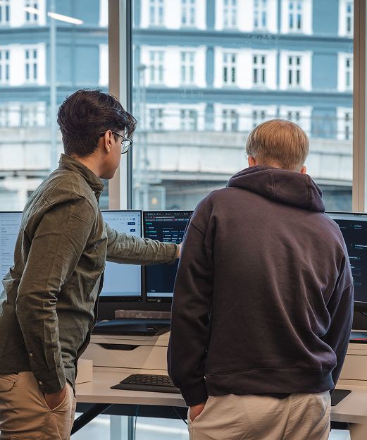 Two colleagues reviewing code on multiple monitors at an office desk.