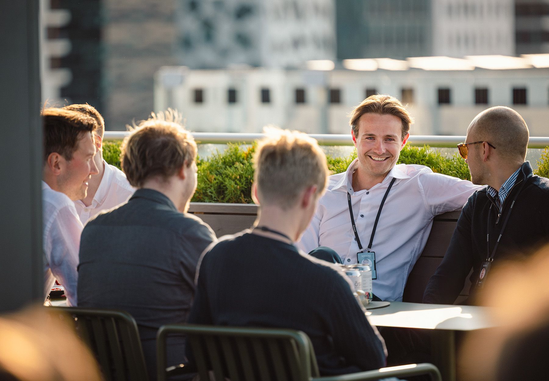 Colleagues sitting outdoors at a table, talking and smiling in the sunlight.
