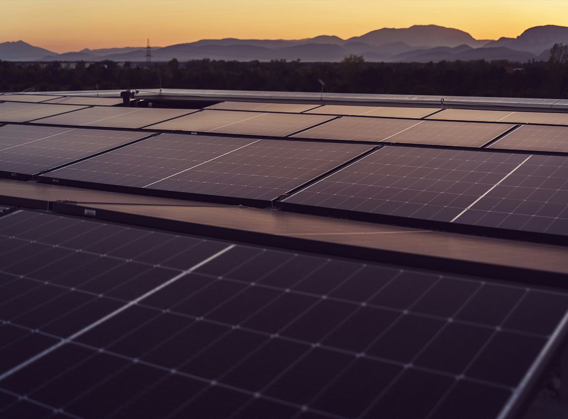 Solar panels on a rooftop with mountains and sunset in the background.