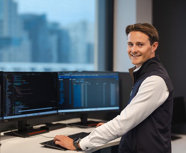 Person ved et skrivebord bruker to skjermer med kode og programvare åpne.