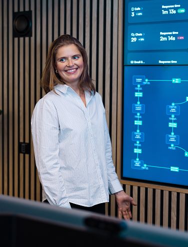 Person in a striped shirt standing in front of a large screen displaying technical graphs and data.