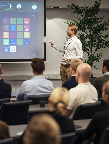 Man giving a presentation to a seated audience in a meeting room.