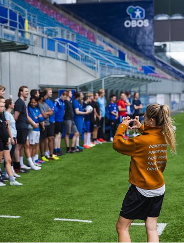 Woman making a heart with her hands towards a group on a soccer field in a stadium.